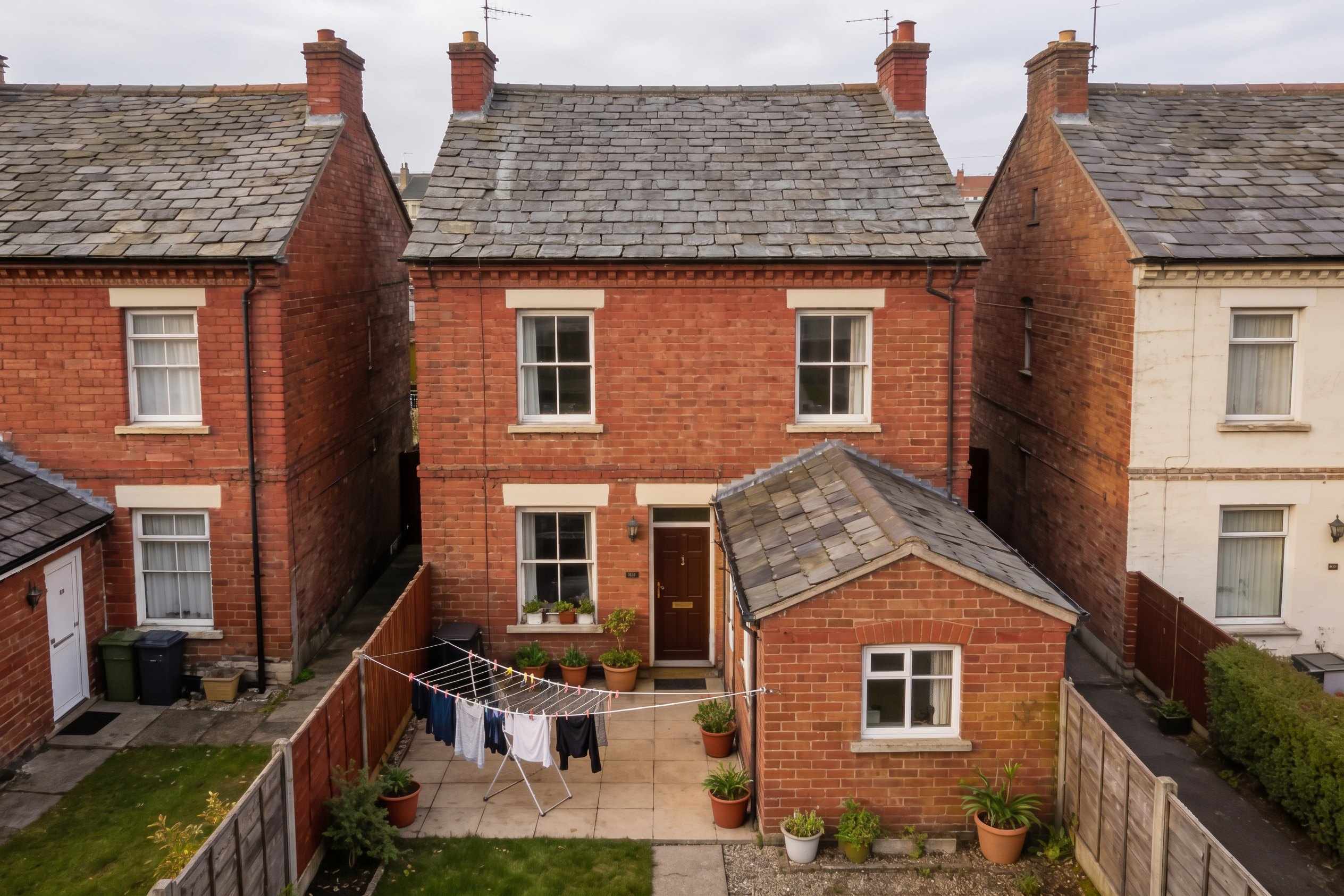The back of a red brick Victorian terraced house under a grey sky, its rear slate roof plain, a small garden with a washing line