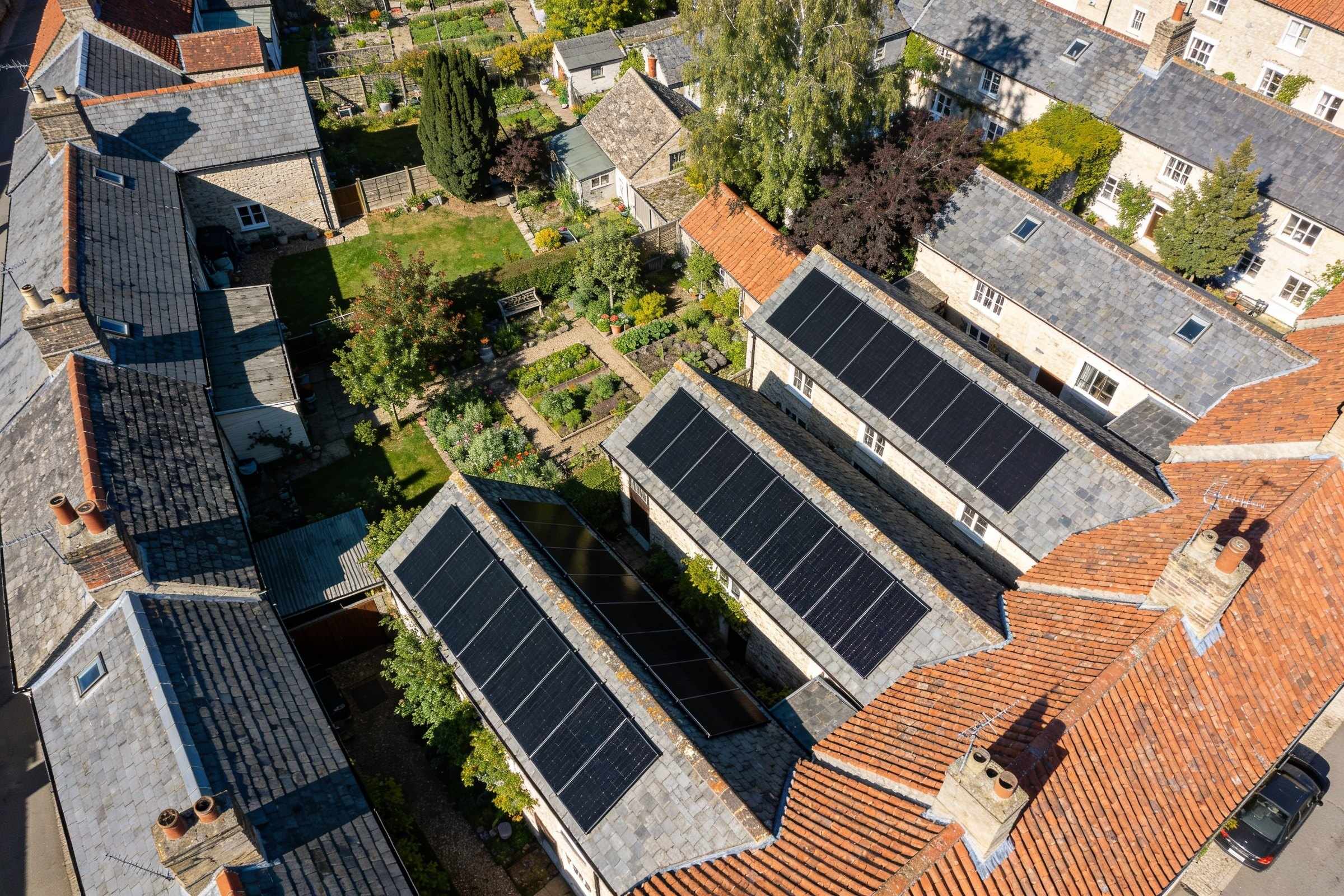 Village rooftops from above, grey slate and red tile, several south-facing slopes covered in neat rectangles of black solar panels